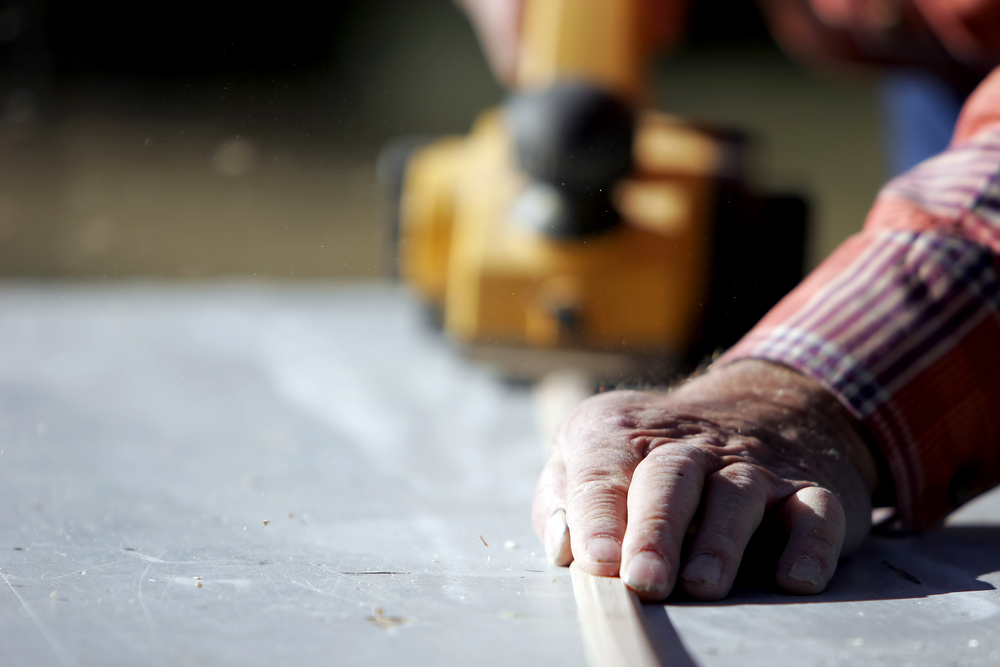 Construction,worker,planing,a,piece,of,wood,for,a,building